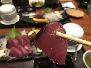 いけす料理『なにわ』の【びやびやかつお】の刺身を一切れ箸で摘み上げた様子